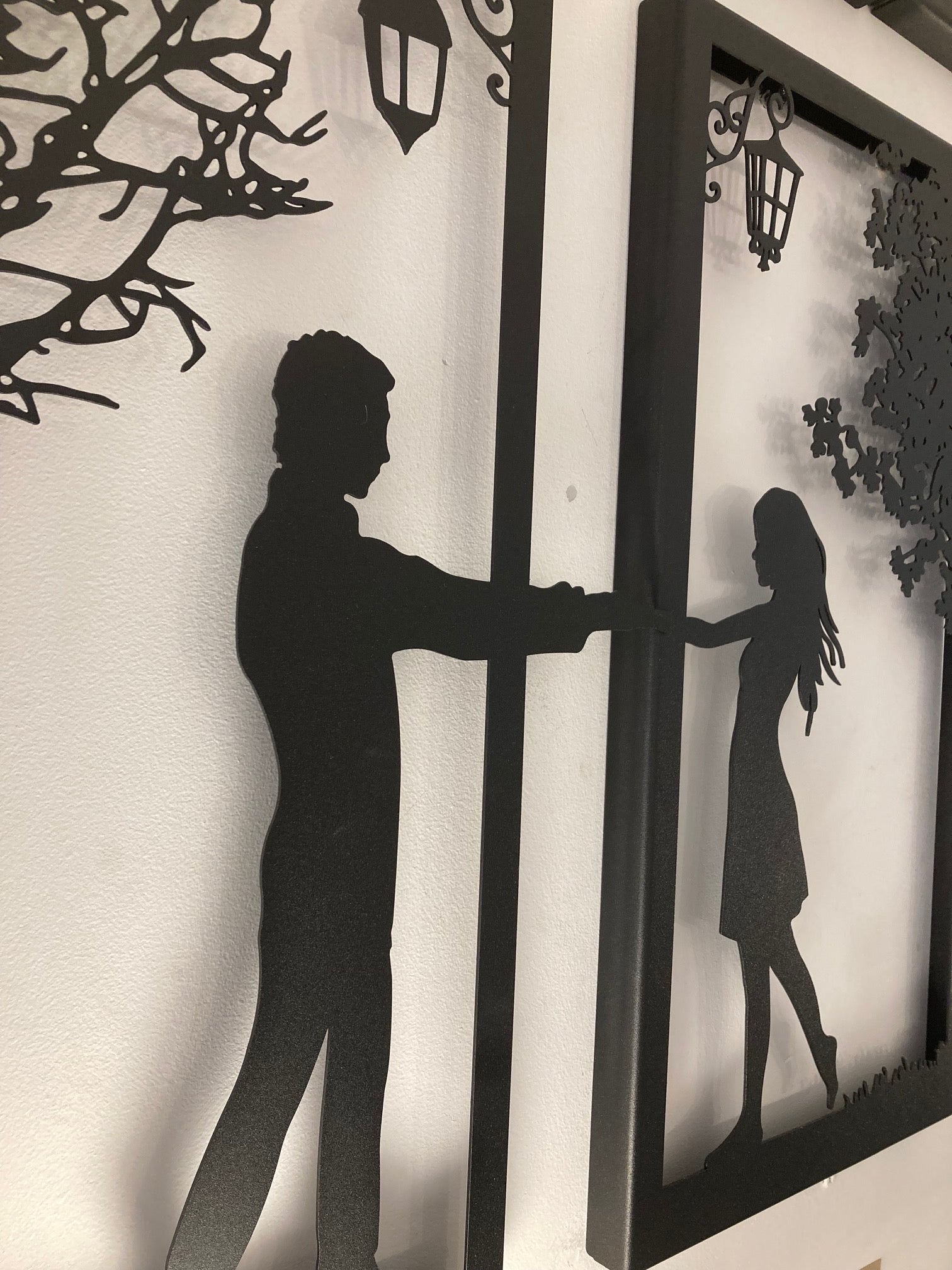 Metal wall art of boy and girl standing under a tree and lamp arms stretched out holding hands