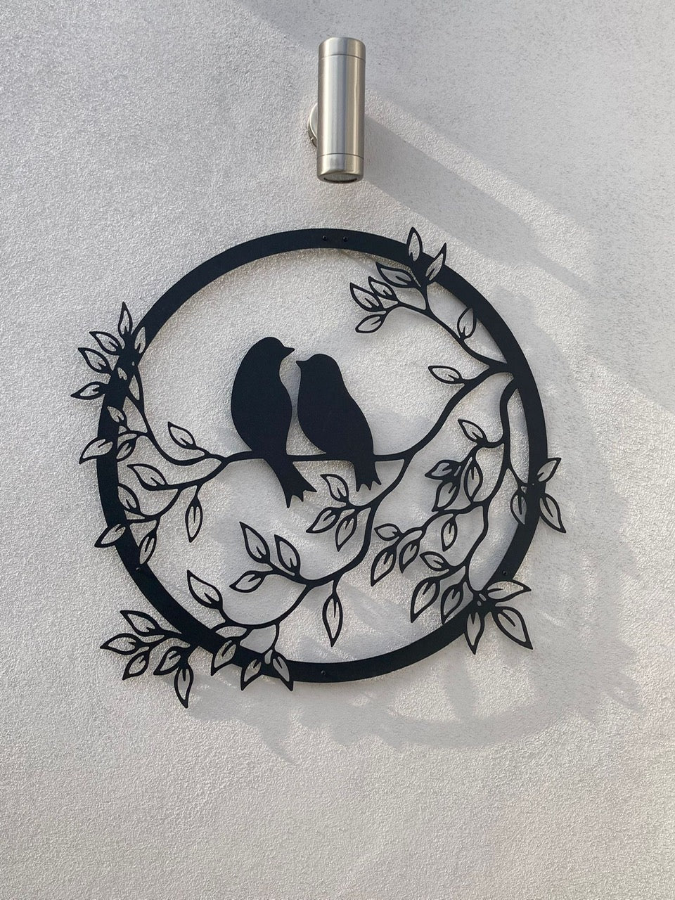 Metal Wall Art two birds siting on a branch looking at each other in a lovinq way with branches and leaves in a circular frame